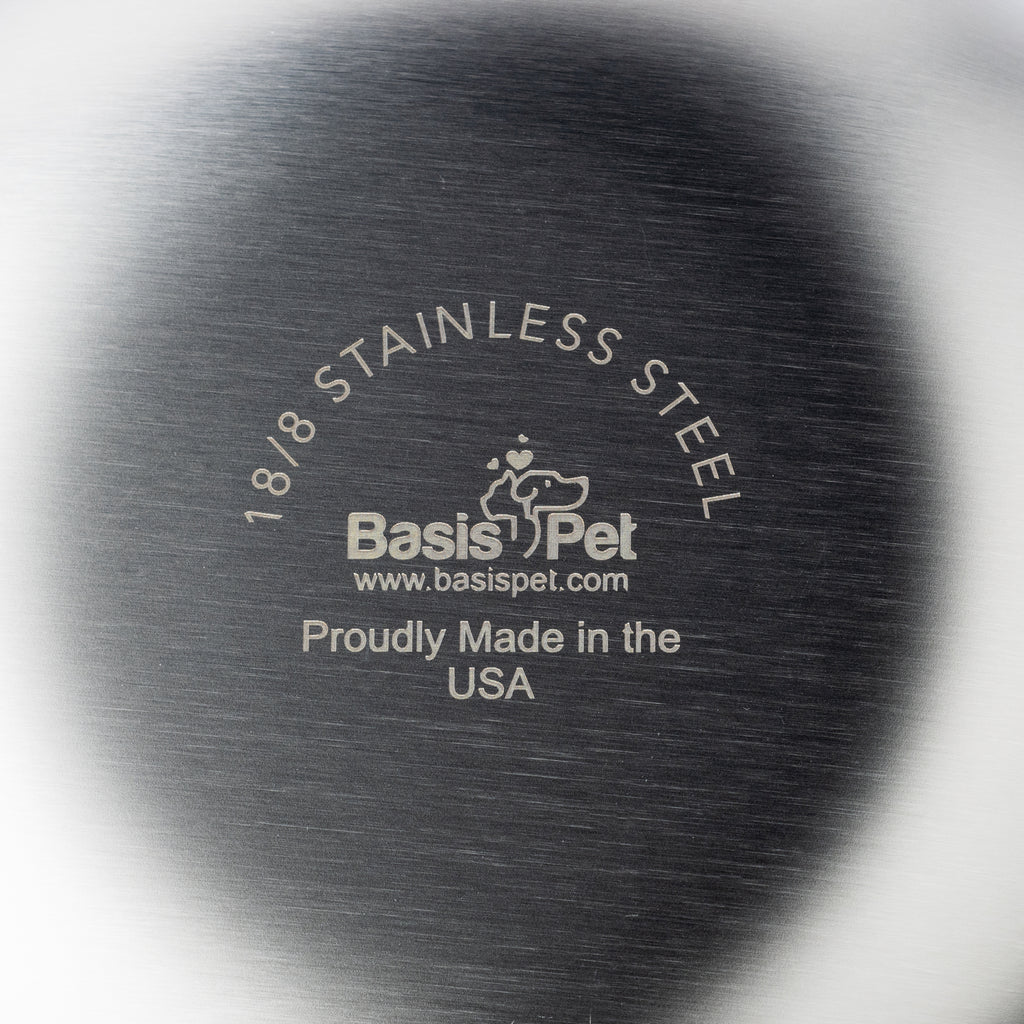 The underside bottom of a Basis Pet stainless steel cat bowl highlighting the Basis Pet logo along with "18/8 Stainless Steel" and "Proudly Made in the USA".