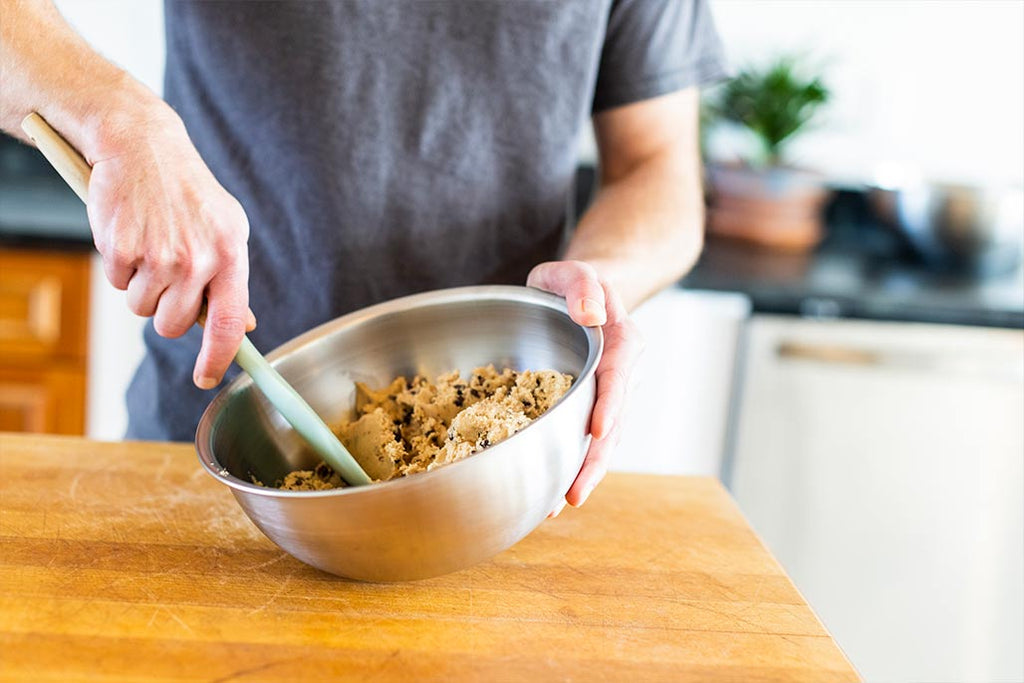 A closeup showing a person mixing cookie dough in a Workhorse Stainless Steel Mixing Bowl.