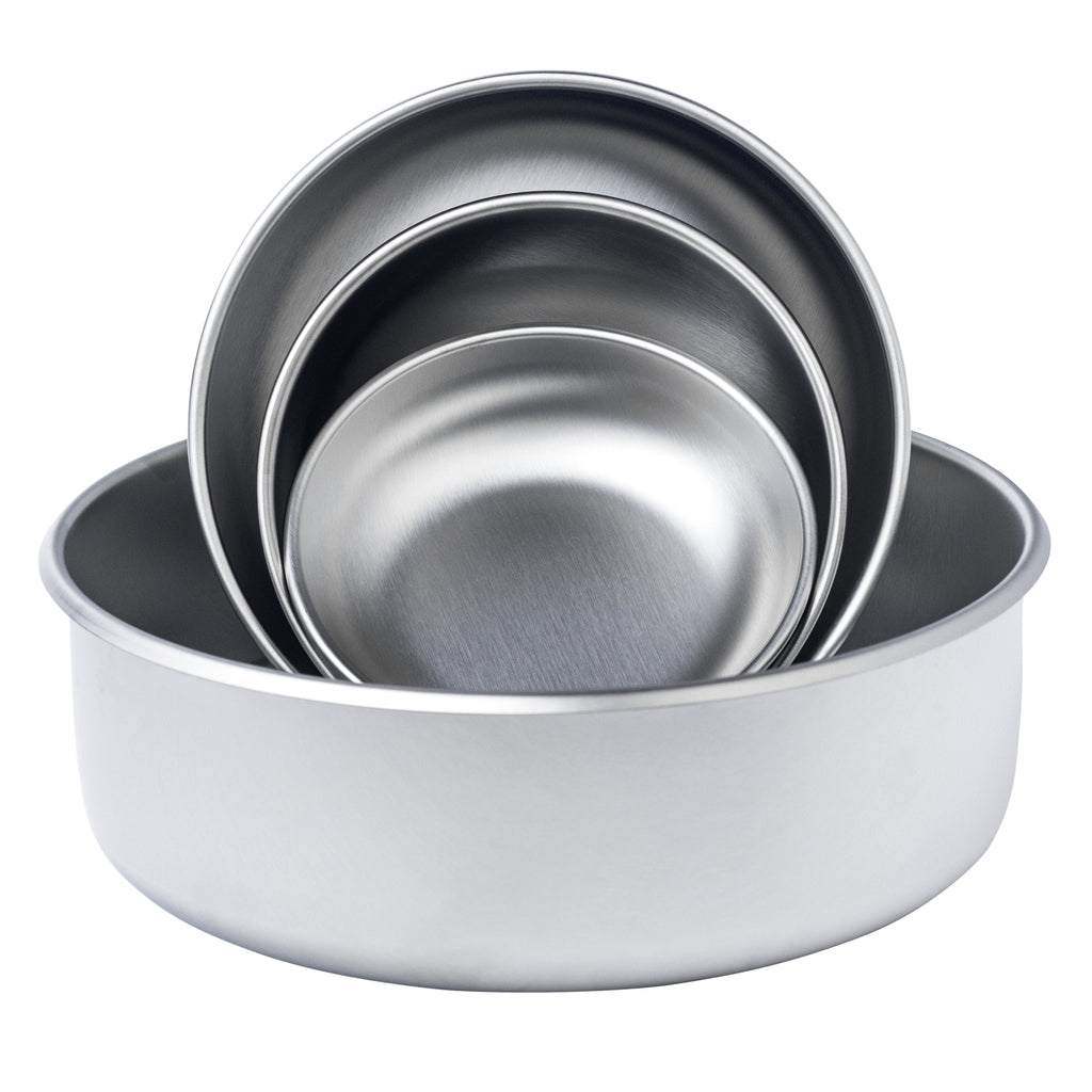 All 4 sizes of the Basis Pet stainless steel dog bowls staged artistically. The extra large size bowl is sitting flat in a normal bowl position while the small, medium, and large size bowls are nested inside one another and shown upright inside the extra large bowl.