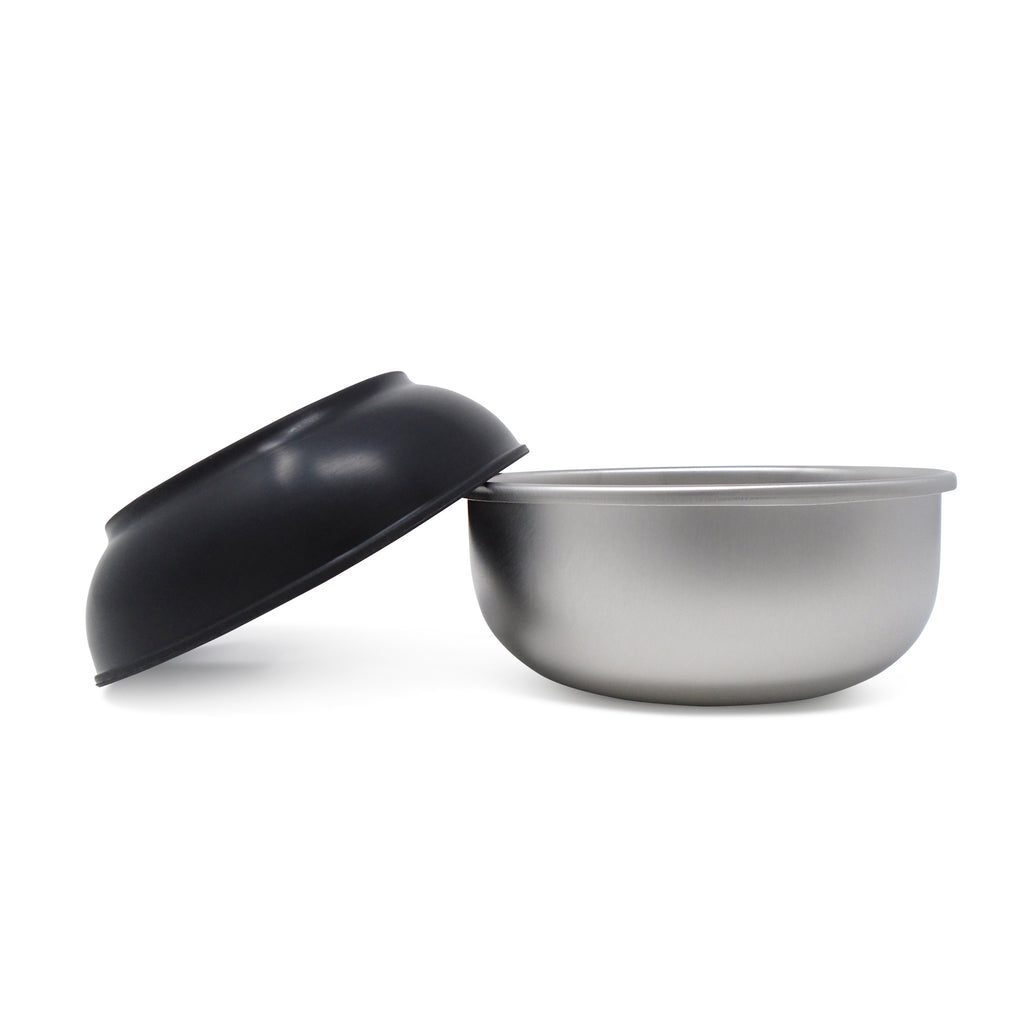 A single size medium Basis Pet stainless steel dog bowl shown upright with a black bowl cozy resting at an angle on the lip of the bowl.