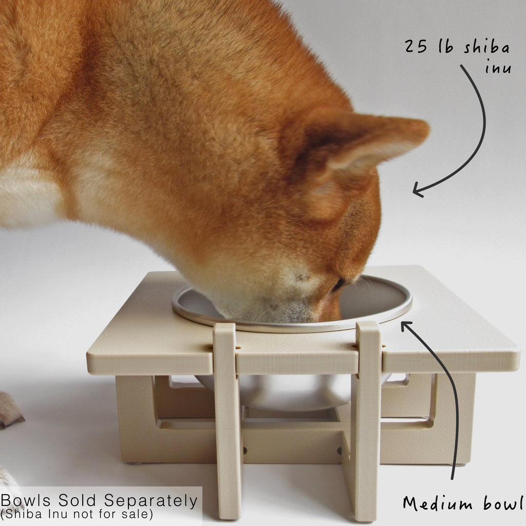 Close-up of a dog eating from a single bowl Rise Pet Bowl Stand for medium dog bowls. Text reads "25 pound shiba inu", "medium bowl", and "bowls sold separately (Shiba Inu not for sale)".